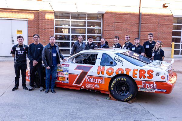 Image shows Kulwicki 1992 team members and Niner Engineer motorsports students with championship car at Kulwicki Lab